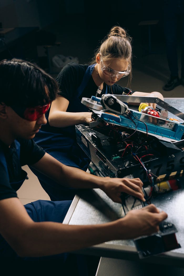 Two young engineers collaboratively work on a robotic assembly indoors.